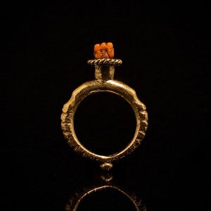May include: A gold ring with a textured band and a small orange stone on top.