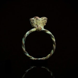 Op de afbeelding: Een gedraaide koperen ring met een decoratief vlinderontwerp aan de bovenkant. De ring is donkergroen van kleur met een patina-afwerking.