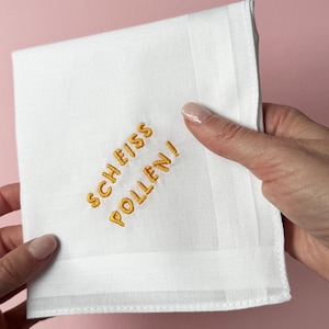 Könnte beinhalten: Weißes Baumwolltaschentuch mit gelbsticktem Text "SCHEISS POLLEN!"