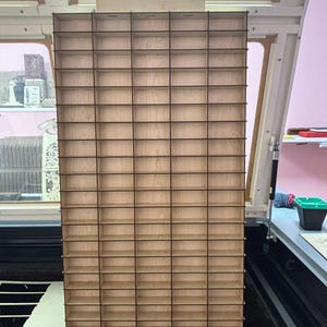 May include: A tall, rectangular wooden storage organizer featuring a grid of numerous small, open compartments. The structure is constructed from light-colored plywood with dark, thin dividers creating a uniform pattern of rectangular cubbies.