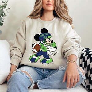 a woman sitting on a couch wearing a mickey mouse sweatshirt