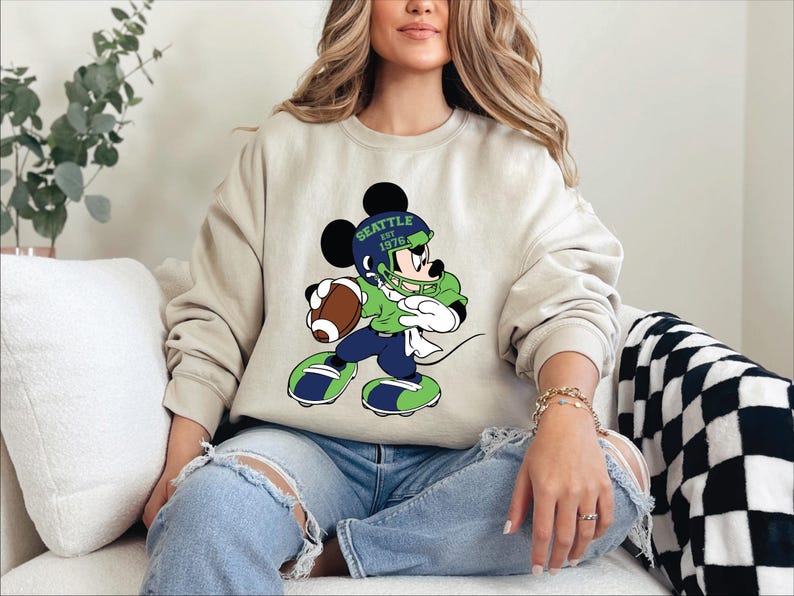 a woman sitting on a couch wearing a mickey mouse sweatshirt