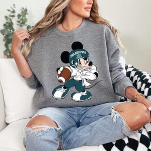 a woman sitting on a couch wearing a mickey mouse sweatshirt