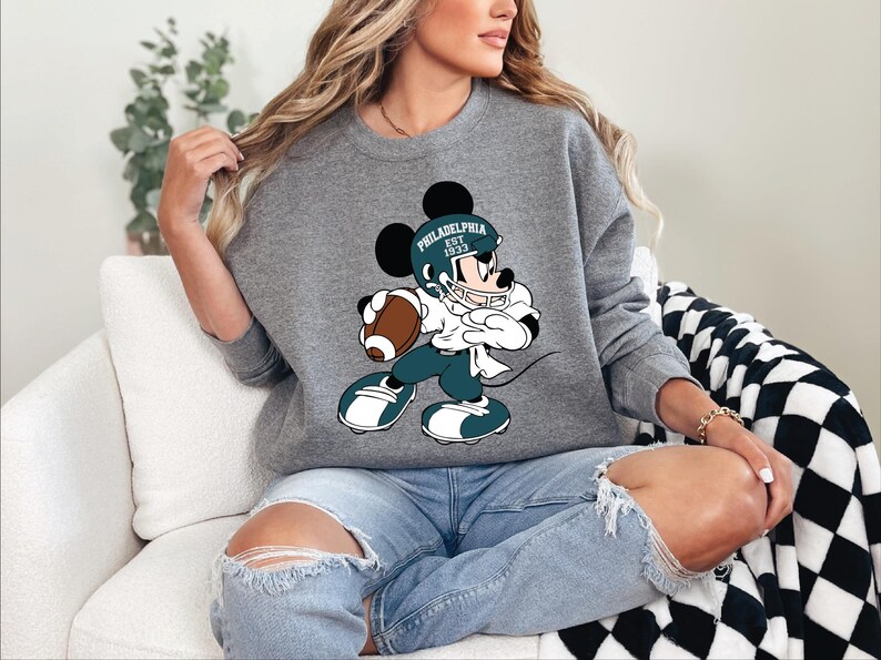 a woman sitting on a couch wearing a mickey mouse sweatshirt
