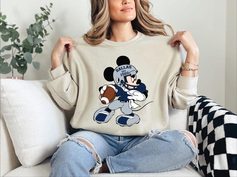 a woman sitting on a couch holding a mickey mouse shirt