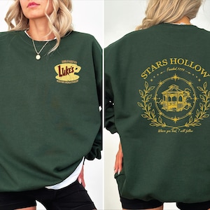 May include: Green sweatshirt with a graphic of Luke's Diner on the front and a graphic of Stars Hollow, founded 1779, with a gazebo and the text "Where you lead, I will follow" on the back.