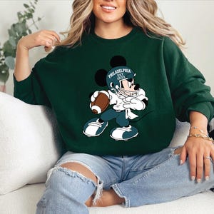 a woman sitting on a couch wearing a mickey mouse sweatshirt