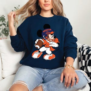 a woman sitting on a couch wearing a mickey mouse sweatshirt
