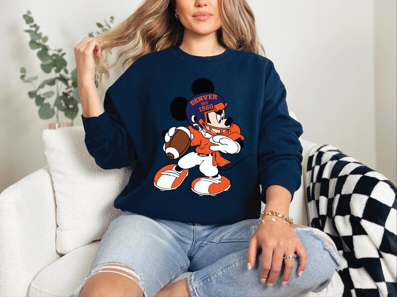 a woman sitting on a couch wearing a mickey mouse sweatshirt