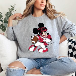 a woman sitting on a couch wearing a mickey mouse sweatshirt
