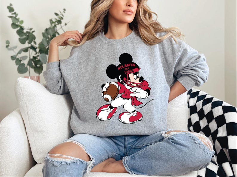 a woman sitting on a couch wearing a mickey mouse sweatshirt