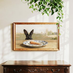 May include: A framed painting shows a black rabbit looking at a carrot on a blue and white plate. The artwork is in a wooden frame, with a rural landscape in the background. Greenery hangs above the painting, adding a natural touch.