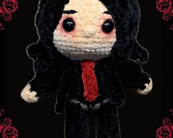 Puede incluir: Muñeca de ganchillo hecha a mano con cabello negro, traje negro y corbata roja. La muñeca tiene piel pálida y ojos negros grandes. Fondo negro con detalles florales rojos y el texto "Static Alley".