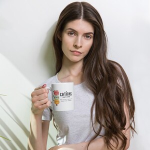 May include: White ceramic mug with a colorful illustration of three cats stacked on top of each other. The text "CATIONS (CAT-IONS) THE CATS IONS WITH POSITIVE CHARGE" is printed on the mug.