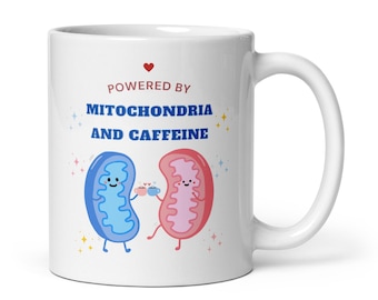May include: White ceramic mug with the text "POWERED BY MITOCHONDRIA AND CAFFEINE" in red and blue. The mug features cartoon illustrations of a blue and pink mitochondria holding coffee cups. A red heart is above the text.