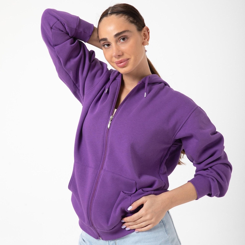 May include: A solid purple zip-up hoodie featuring a drawstring hood, long sleeves with ribbed cuffs, and two front pockets. The garment is constructed from a smooth, opaque fabric and includes a silver-toned metal zipper closure down the center.