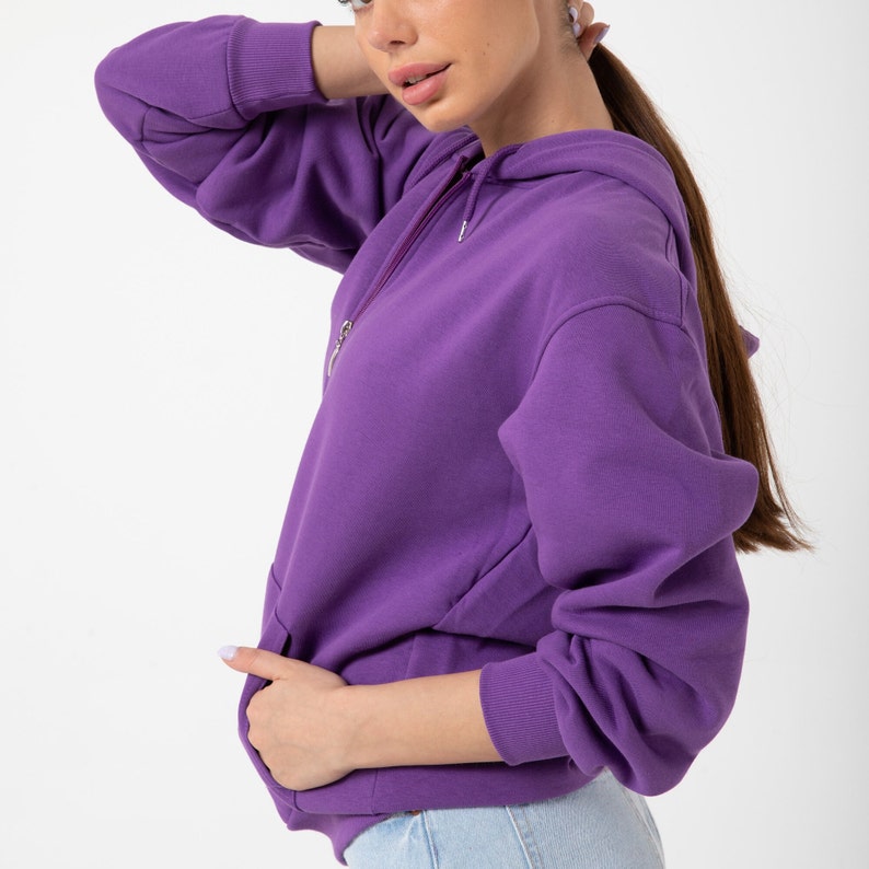 May include: A purple hooded sweatshirt with a zip fastening. The sweatshirt has a kangaroo pocket and long sleeves.