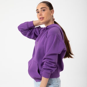 May include: A purple hooded sweatshirt with a zip fastening and a kangaroo pocket. The sweatshirt is made from a soft, comfortable fabric.