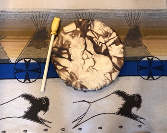 May include: A brown leather hand drum with a marbled pattern and a wooden stick. The drum is on a beige and blue patterned rug.