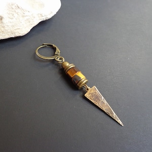 Peut inclure: Une boucle d'oreille dorée avec une perle en œil de tigre et un pendentif triangulaire.