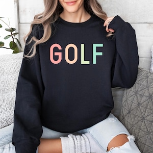 Pode incluir: Camisola de moletom preta com a palavra "GOLF" impressa em cores do arco-&iacute;ris.