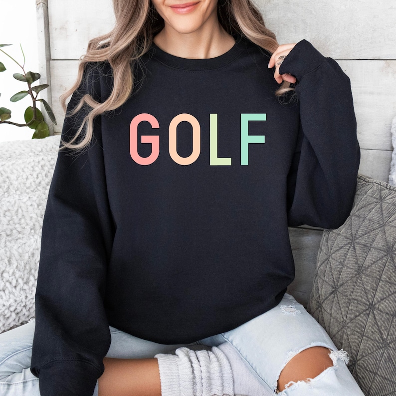 Pode incluir: Camisola de moletom preta com a palavra "GOLF" impressa em cores do arco-&iacute;ris.