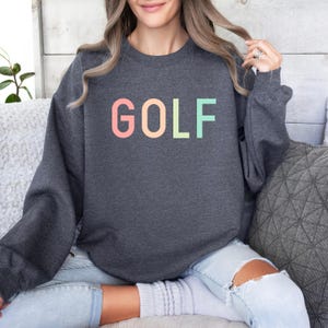 Pode incluir: Uma camisa de moletom cinza escuro com a palavra "GOLF" impressa em cores do arco-&iacute;ris no peito.