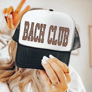 Puede incluir: Gorra de camionero en blanco y negro con la inscripción "BACH CLUB" en estampado de leopardo. La gorra tiene la parte trasera de malla y una visera curvada. Un accesorio divertido para una despedida de soltera.