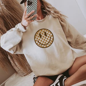 Peut inclure: Un sweat-shirt beige avec un motif de smiley visage à carreaux. Le sweat-shirt est fait d'un matériau doux et confortable et a une coupe décontractée.
