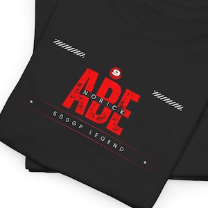 Puede incluir: Camiseta negra con un gráfico rojo de la palabra "ABE" con "NORICK" escrito dentro de las letras. El número "9" está por encima del gráfico. El texto "500GP LEGEND" está debajo del gráfico.