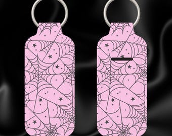 May include: Two pink keychains with a silver ring. Each keychain features a black spiderweb design with stars. One keychain has a slot. The keychains are designed for holding a small item.