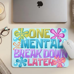 May include: A light blue rectangular mousepad with the text "ONE MENTAL BREAK DOWN LATER" in colorful bubble letters. The design includes cartoon starfish and bubbles. A white mouse and a laptop are visible.