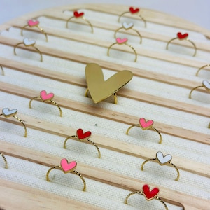 Può includere: Un espositore per anelli in legno con anelli in oro con cuori smaltati in rosso, rosa e bianco.