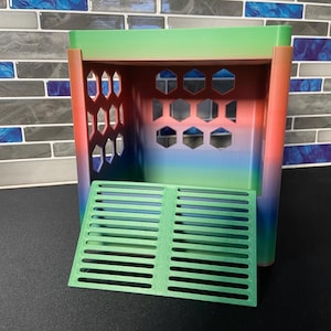 May include: A 3D printed enclosure featuring a gradient color scheme transitioning from green to orange, red, purple, and blue. The structure has hexagonal cutouts on the sides and back, and includes a separate green rectangular ramp with slats.