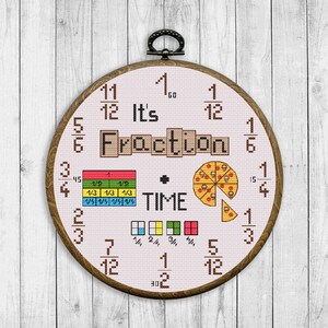 May include: A cross-stitch embroidery in a wooden hoop. The design features the words "It's Fraction Time" with fraction examples, a pizza, and a clock-like arrangement of numbers. The hoop is approximately 20 cm in diameter.