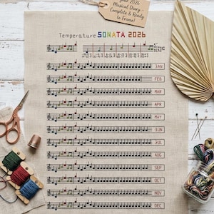 Puede incluir: Un diario musical de tela beige para 2026, con notas musicales bordadas a punto de cruz y el texto "Temperature SONATA 2026." Incluye los meses de enero a diciembre. Se ven accesorios como tijeras, carretes de hilo y un dedal.