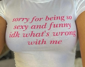 Op de afbeelding: Witte crop top met roze tekst die "sorry for being so sexy and funny idk what's wrong with me" zegt.