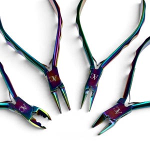 May include: A set of four metal pliers featuring an iridescent rainbow finish. Each tool has a distinct head shape, including needle-nose and cutting styles, with the letters AC engraved on the joint of every piece.