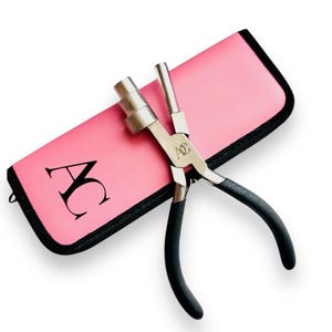 May include: A pink carrying case with the letter "AC" printed on it, and a pair of silver and black pliers with black rubber handles.