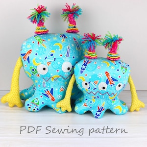 May include: Two blue plush toys with rocket ship and star patterns. The larger toy has yellow arms and the smaller toy has yellow arms and legs. Both toys have colorful yarn hair.