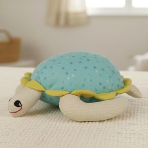 Può includere: Un peluche a forma di tartaruga con un guscio azzurro chiaro a fantasia di stelle bianche. La tartaruga ha finiture gialle, arti color crema e un viso sorridente. Un giocattolo morbido per bambini.