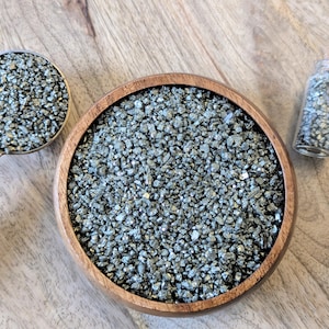 May include: A wooden bowl filled with silver glitter, a small scoop of glitter, and a glass bottle with a cork stopper filled with silver glitter.