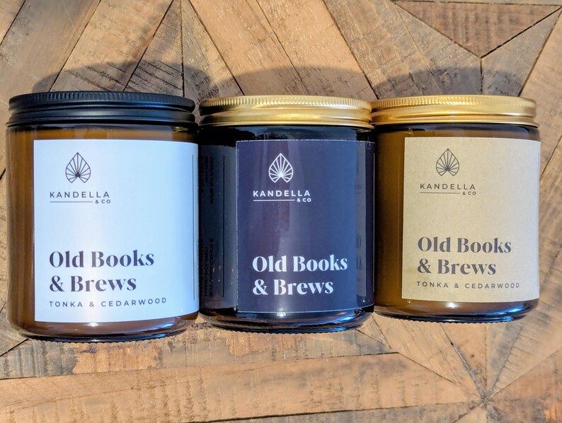 May include: Three glass jar candles with black, gold, and silver lids. Each jar has a label with the text "Old Books & Brews" and the brand name "Kandella & Co." The labels are white, navy blue, and tan.