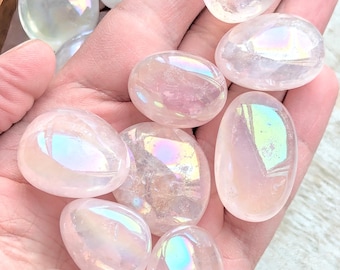 May include: A collection of iridescent, white, and pink tumbled stones. The stones have a smooth, polished finish and are arranged in a hand.
