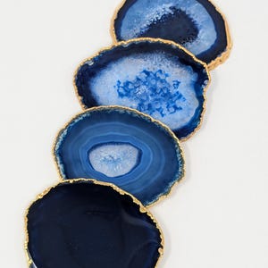 May include: Four blue agate coasters with gold trim. The coasters are round and have a natural, organic shape. They are perfect for adding a touch of elegance to any home.