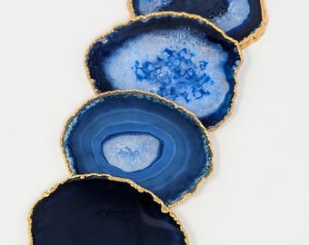 May include: Four blue agate coasters with gold trim. The coasters are round and have a natural, organic shape. They are perfect for adding a touch of elegance to any home.