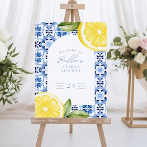 May include: Welcome to Bella's Bridal Shower sign with a blue and white tile pattern, lemons, and green leaves. The sign says "Welcome to Bella's Bridal Shower" and "Sat 24 Aug".