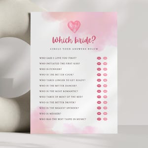 Op de afbeelding: Een roze en witte aquarel achtergrond met een roze hart bovenaan. De tekst "Which bride?" is in zwarte tekst. De tekst "Circle your answers below" is in zwarte tekst. Een lijst met vragen over de bruiden is in zwarte tekst met roze lippen naast elke vraag.