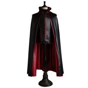 May include: A black satin cape with a red satin trim and a red lace-up detail at the front. The cape is on a mannequin.