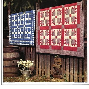 May include: Two quilts hanging on a wooden fence. The quilt on the left is blue with white paw prints. The quilt on the right is red with white paw prints.